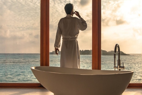 Tips To Save On Bathroom Plumbing Renovations - man in a bathroom robe looking over the view in his modern bathroom with a bathtub